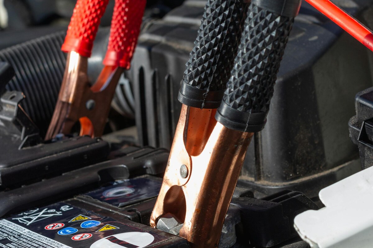 Pacific Unlocks jump start service Honolulu — red and black jumper cable clamps connected to a dead car battery for roadside boost in Waikiki, Oahu